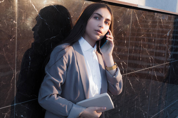 Young attractive girl in business suit uses phone. Lifestyle and business portrait - Foto, Imagem