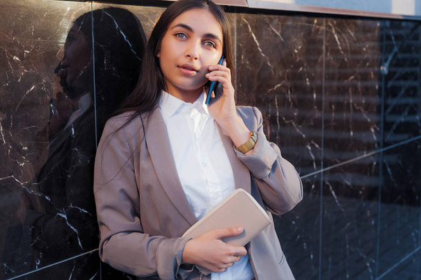 Young attractive girl in business suit uses phone. Lifestyle and business portrait - Foto, Imagem