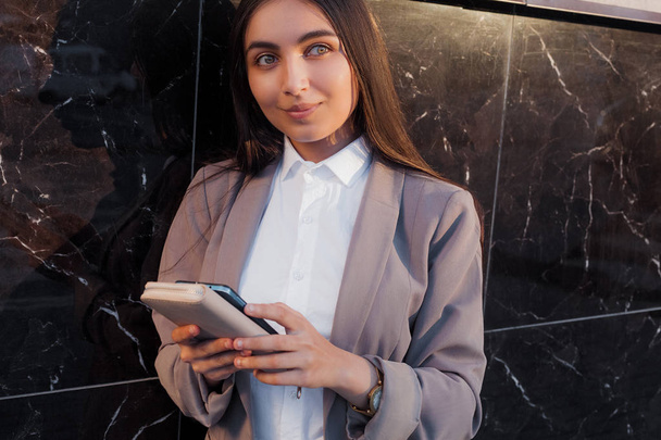 Young attractive girl in business suit uses phone. Lifestyle and business portrait - Foto, imagen
