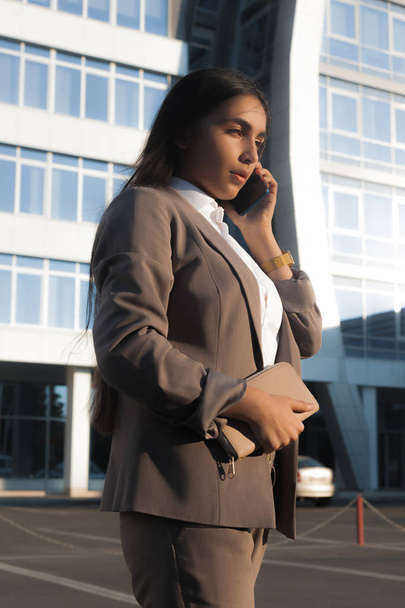 Young attractive girl in business suit uses smartphone. Lifestyle and business portrait - Фото, изображение