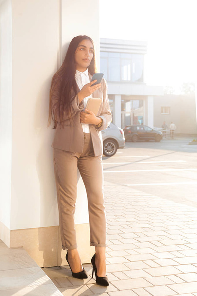 Young attractive girl in business suit uses smartphone. Lifestyle and business portrait - 写真・画像