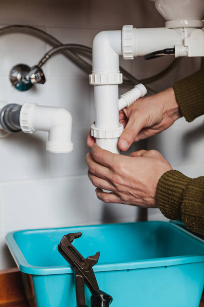 handen van het sanitair ontmantelen de keuken hydraulische rolluiken systeem close-up. Vlakbij de pijpschroef - Foto, afbeelding