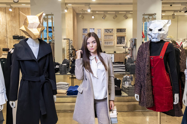 Beautiful serious young brunette girl in a clothing store near mannequins with animal masks. The concept of shopping and fashion. - Photo, Image