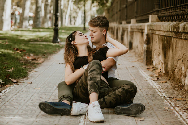 Jovem casal amoroso ao ar livre sentado na grama e abraçando adolescentes
 - Foto, Imagem