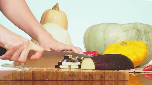 Frauenhände schneiden mit einem Messer eine Aubergine. Gemüsemischung zum Kochen von Gemüseeintopf. Hintergrundfarbe. das Konzept der gesunden Ernährung und Ernte. - Foto, Bild