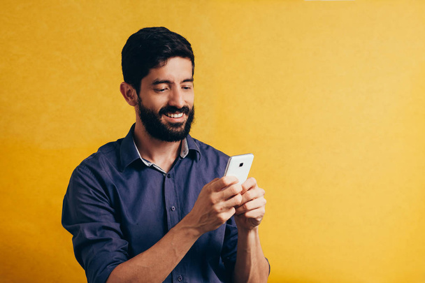 Portrait of young using mobile phone isolated over yellow background - Foto, Imagen