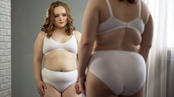Obese female attentively looking at her reflection in mirror, body positive - Foto, Imagen