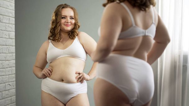 Body positive plump girl looking in mirror, admiring her appearance, femininity - Foto, Imagem