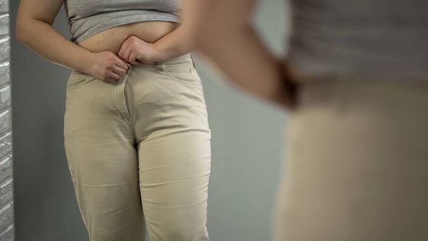 Obese lady trying to button tight pants, overweight body problem, closeup - Foto, Imagem
