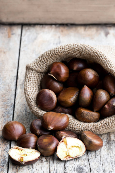 Fresh  chestnuts in sack bag on the old wooden table  - Photo, Image
