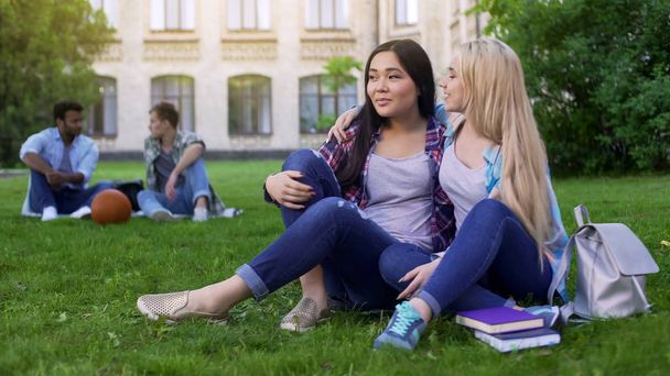 Best friends sitting on lawn near college, hugging, support and friendship - Foto, imagen