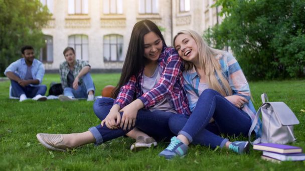 Young beautiful women sitting on lawn near college, laughing and gossiping - Foto, Imagen