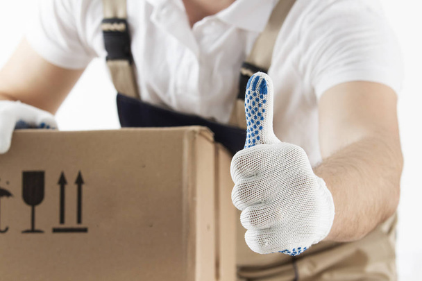 Delivery concept. Courier holds his thumb up. Man with cardboard box close-up. Relocation services. Loader with a box. Mover in uniform with parcel. - Zdjęcie, obraz