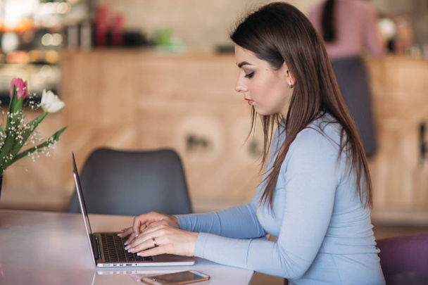 Mooie brunette vrouw gebruik bedrijfstelefoon in een café met laptop - Foto, afbeelding