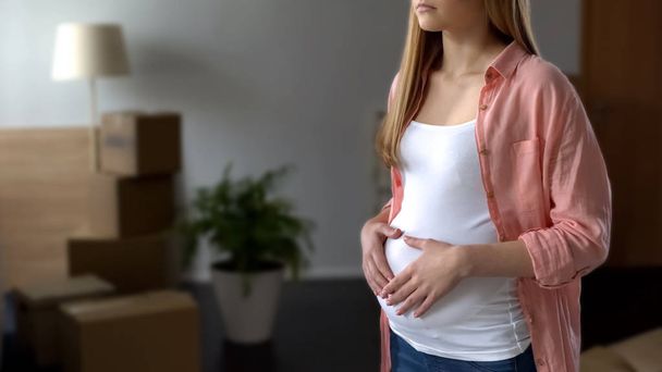 Unhappy pregnant woman lost apartment, things in boxes on background, poverty - Foto, imagen