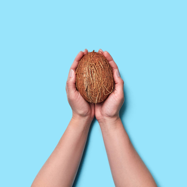 La noix de coco tropicale tient les mains des femmes sur un fond bleu avec de l'espace pour le texte. Aménagement alimentaire. Pose plate
 - Photo, image