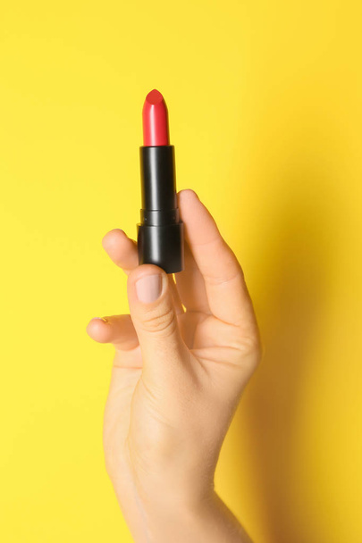 Woman holding bright lipstick on color background - Fotó, kép