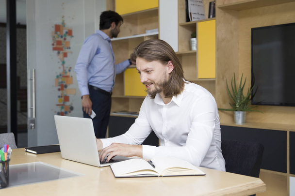 Udany młody biznesmen, wpisując na laptopie w nowoczesnym biurze - Zdjęcie, obraz
