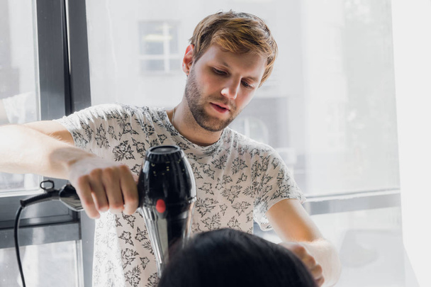 Usmívající se muže stylista sušení Zenske vlasy se sušičkou v salonu Professional - Fotografie, Obrázek