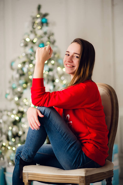 Счастливая молодая женщина сидит возле рождественской елки. - Фото, изображение