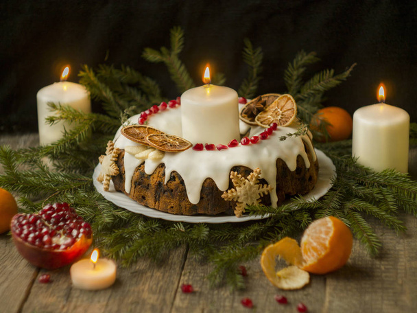 Christmas English fruitcake with candied fruit, dried fruit and nuts, decorated with white icing on a wooden background with fir branches, candles. Festive English cuisine - Fotó, kép