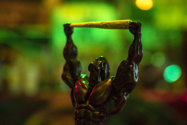 Αγαλματίδιο φιγούρα του μυώδης άνδρας τροχαίο κατέχουν Προ-κυλημένα μαριχουάνα κοινή σε φωτεινό πράσινο neon φόντο στο νυχτερινό κέντρο - Φωτογραφία, εικόνα