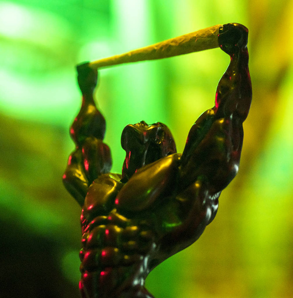 Estatuilla figura de muscular Rolling man hold Pre-enrollado marihuana conjunta sobre fondo de neón verde brillante en el club nocturno
 - Foto, Imagen
