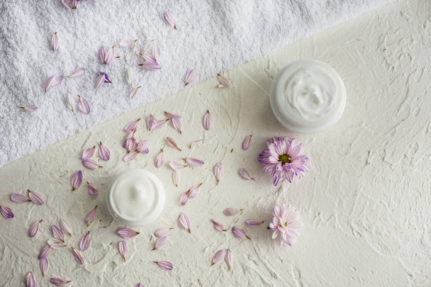 Jars with body cream, flower petals and soft towel on white table - Foto, Bild
