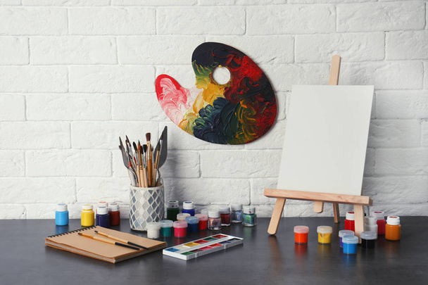 Easel with various artist tools on table against brick wall. Space for text - Photo, image