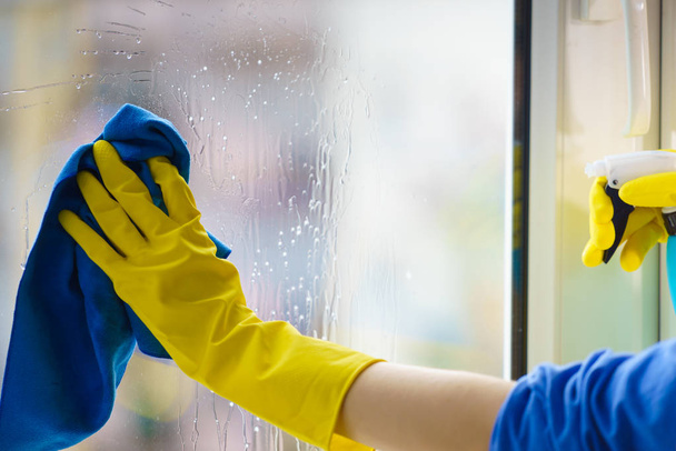 Female hand in yellow gloves cleaning window pane with rag and spray detergent. Cleaning concept - Fotoğraf, Görsel