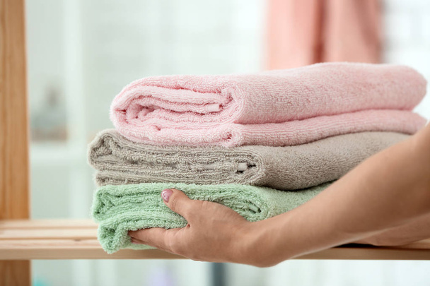 Woman putting stack of clean towels on shelf in bathroom - Foto, Bild