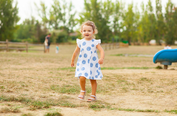 Menina bonita com cabelo loiro e olhos azuis joga ao ar livre em um dia de verão
. - Foto, Imagem