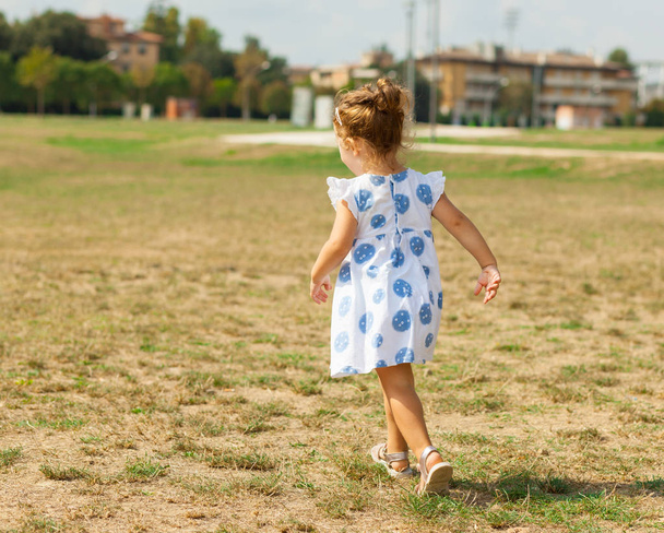 Menina bonita com cabelo loiro e olhos azuis joga ao ar livre em um dia de verão
. - Foto, Imagem