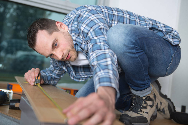 Man measuring laminate flooring - Фото, изображение