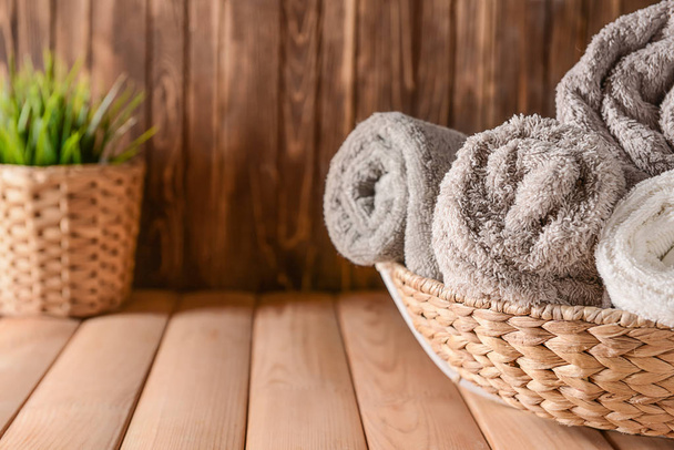 Cesta de mimbre con toallas suaves limpias enrolladas sobre mesa de madera
 - Foto, Imagen