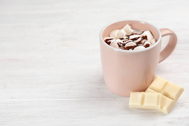 Cup of chocolate milk with marshmallows on light wooden background. Space for text - Photo, image