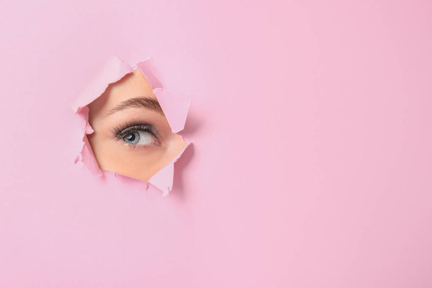 Œil de belle jeune femme visible à travers un trou dans du papier rose déchiré
 - Photo, image