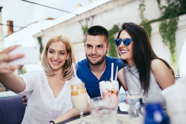 Group of young and attractive three people enjoying private party and making selfie photo. Swimming pool in background. Man with two beautiful women. - Fotografie, Obrázek