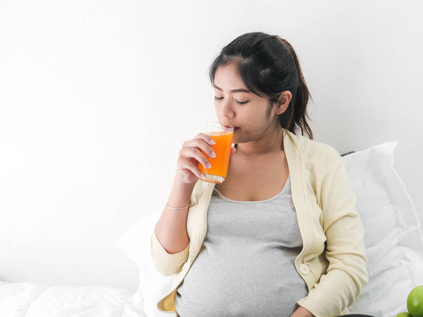 Asian pregnant woman drinking a glass of orange juice, lifestyle concept. - Фото, зображення