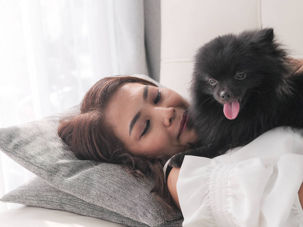 Счастливая азиатская женщина, играющая со своей черной собакой на диване дома, концепция образа жизни
. - Фото, изображение