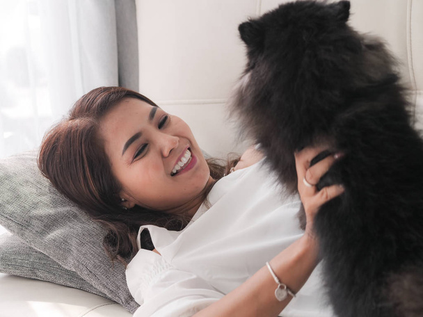 Feliz mujer asiática jugando con su perro negro en el sofá en casa, concepto de estilo de vida
. - Foto, Imagen