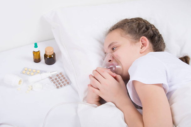 Mädchen im Bett, beim Inhalieren, im Bett eine Maske aufsetzen und Medikamententabletten ansehen - Foto, Bild