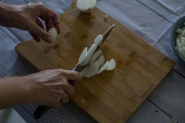 woman  with knife cutting onion on wooden cutting board, close-up  - Photo, Image