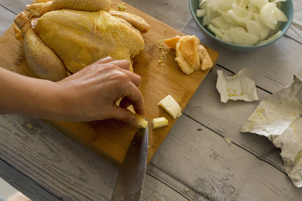 женские руки держат нож и режут масло во время приготовления сырой курицы
 - Фото, изображение