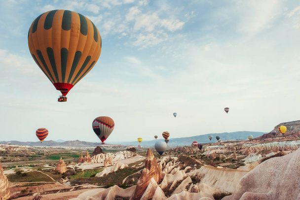 Hot air balloon flying over rock landscape at Cappadocia Turkey. Valley, ravine, hills, located between the volcanic mountains in Goreme National Park. - 写真・画像