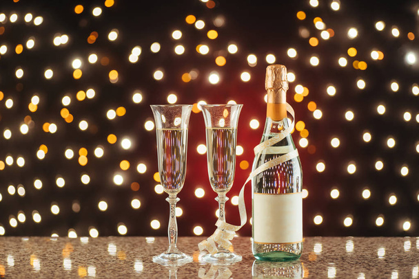 Christmas and New Year celebration with champagne. Pair of flute and bottle of Champagne for festive occasions against a dark background with gold shimmering light and bokeh - Fotó, kép