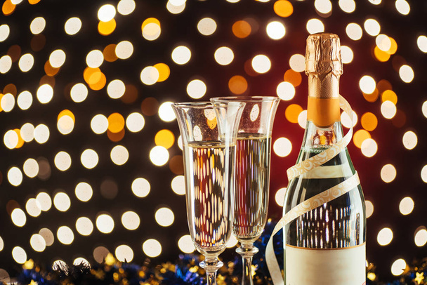 Christmas and New Year celebration with champagne. Pair of flute and bottle of Champagne for festive occasions against a dark background with gold shimmering light and bokeh - Photo, Image