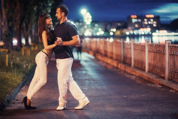 young couple dancing tango on the embankment of the river in the evening - Photo, image