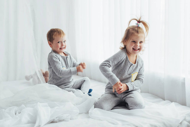 Children in soft warm pajamas playing in bed - Fotografie, Obrázek