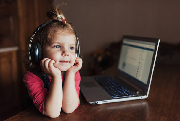 Happy beautiful child in headphones listening to music. In the background a laptop. - Photo, image